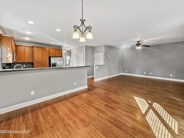 kitchen with pendant lighting, ceiling fan with notable chandelier, stainless steel appliances, and dark wood-type flooring