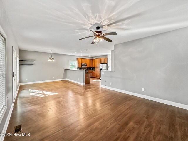 unfurnished living room with ceiling fan with notable chandelier and wood-type flooring