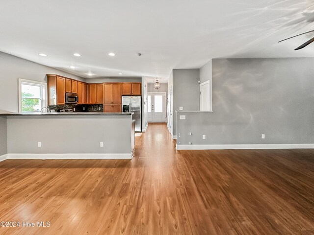 kitchen featuring kitchen peninsula, appliances with stainless steel finishes, tasteful backsplash, ceiling fan, and light hardwood / wood-style flooring