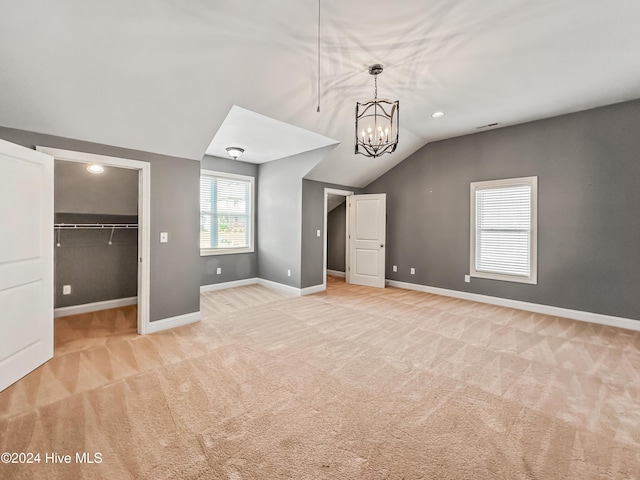 unfurnished bedroom with a spacious closet, light colored carpet, a chandelier, vaulted ceiling, and a closet