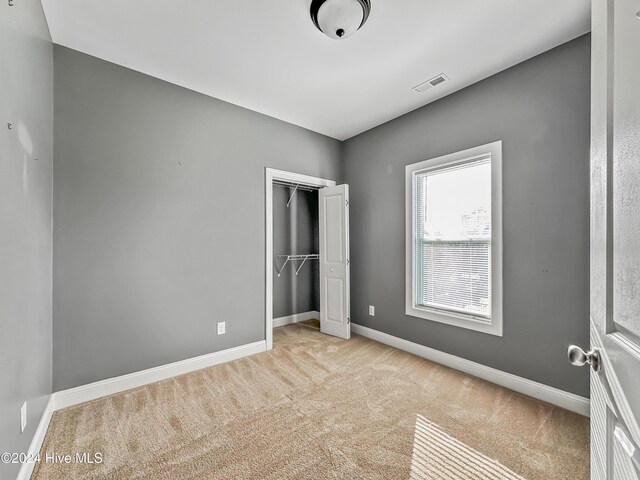 unfurnished bedroom featuring a closet and light colored carpet