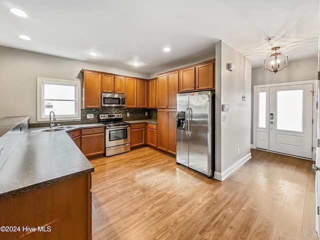 kitchen featuring appliances with stainless steel finishes, sink, pendant lighting, a chandelier, and light hardwood / wood-style floors