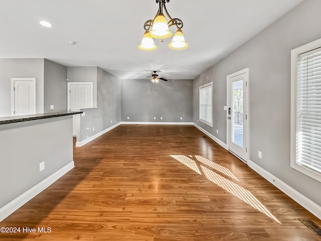 unfurnished dining area featuring ceiling fan with notable chandelier and dark wood-type flooring