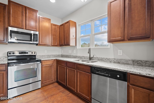 kitchen with stainless steel appliances, light stone countertops, sink, and light hardwood / wood-style floors