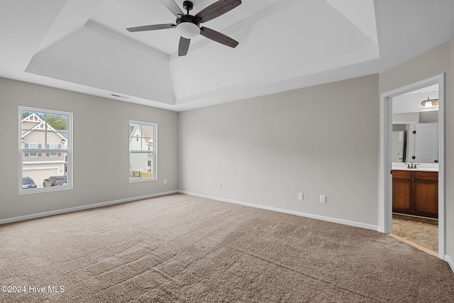 carpeted empty room featuring a raised ceiling, sink, and ceiling fan