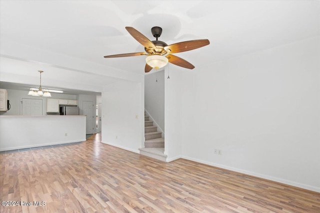 unfurnished living room featuring ceiling fan with notable chandelier and light wood-type flooring