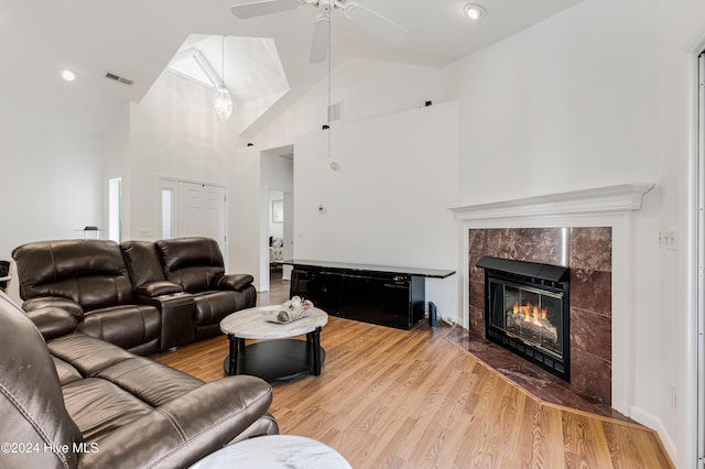 living room featuring a skylight, ceiling fan, light hardwood / wood-style flooring, high vaulted ceiling, and a tiled fireplace