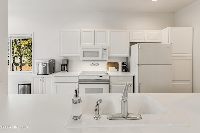 kitchen featuring backsplash, white cabinetry, sink, and white appliances