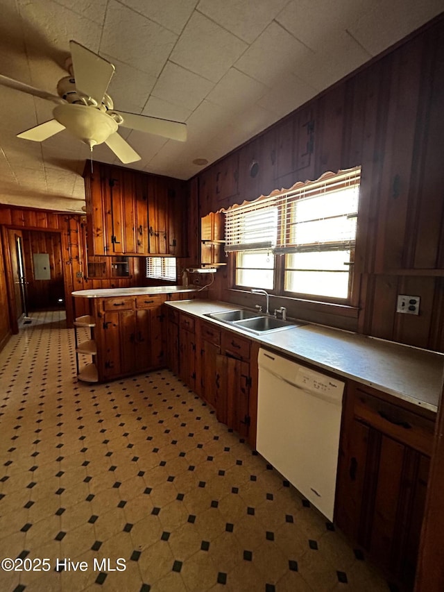 kitchen with dishwasher, ceiling fan, wood walls, and sink