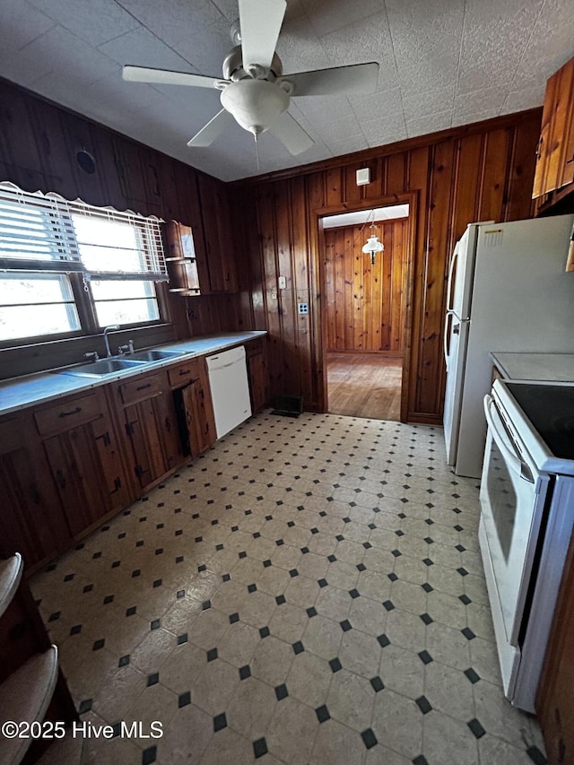 kitchen featuring ceiling fan, white appliances, sink, and wooden walls