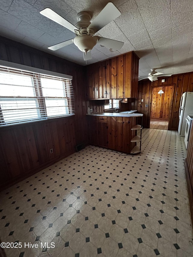 kitchen with white fridge, ceiling fan, wood walls, and kitchen peninsula