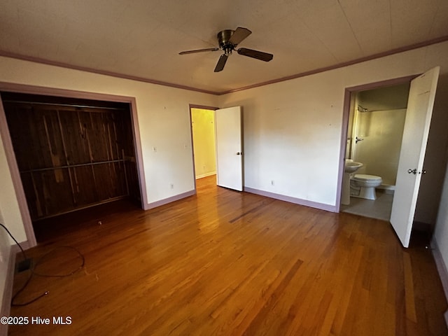 unfurnished bedroom featuring ensuite bath, ceiling fan, ornamental molding, wood-type flooring, and a closet