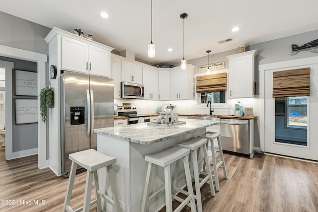 kitchen featuring appliances with stainless steel finishes, light wood-type flooring, pendant lighting, white cabinetry, and a kitchen island