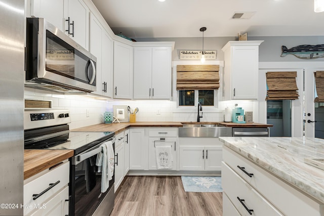 kitchen featuring tasteful backsplash, stainless steel appliances, sink, white cabinets, and hanging light fixtures