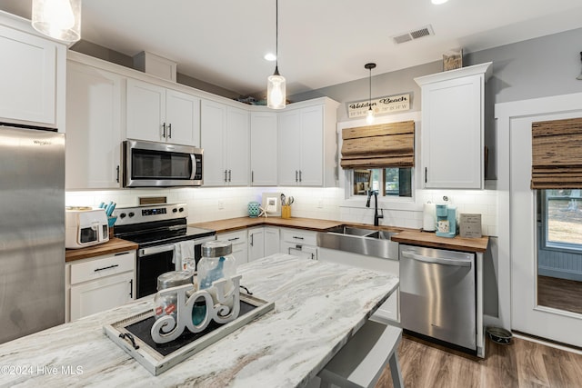 kitchen featuring pendant lighting, white cabinets, appliances with stainless steel finishes, and wooden counters