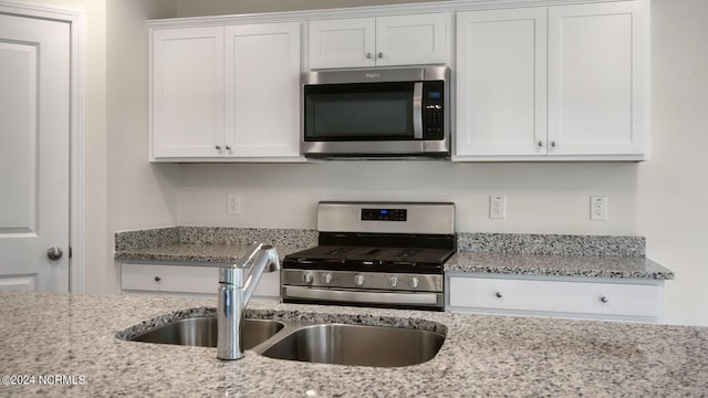 kitchen featuring light stone counters, stainless steel appliances, white cabinetry, and sink