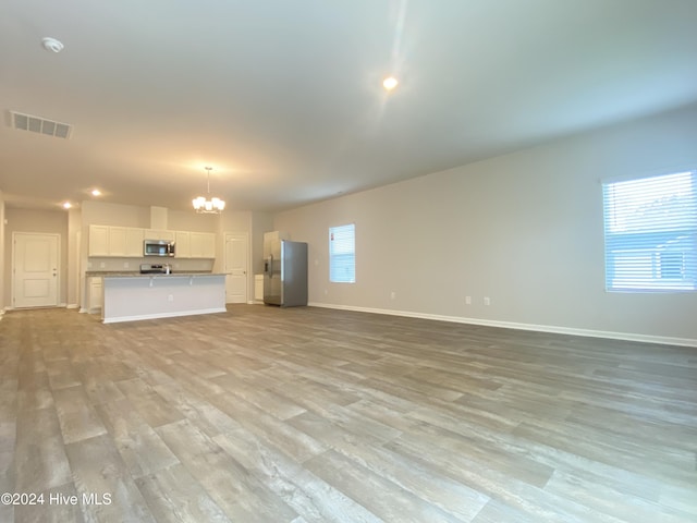 unfurnished living room featuring light wood-type flooring and an inviting chandelier