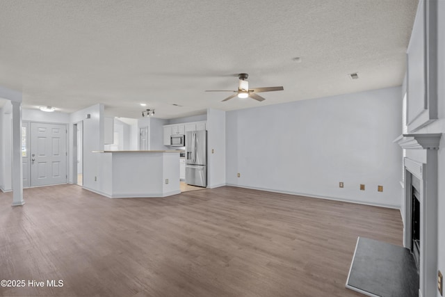 unfurnished living room featuring ceiling fan, light hardwood / wood-style floors, and a textured ceiling