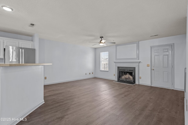 unfurnished living room featuring ceiling fan, dark hardwood / wood-style flooring, and a textured ceiling