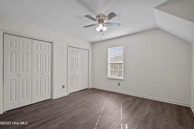 unfurnished bedroom featuring multiple closets, ceiling fan, dark wood-type flooring, a textured ceiling, and lofted ceiling