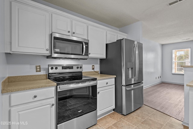 kitchen with a textured ceiling, light tile patterned flooring, white cabinetry, and stainless steel appliances