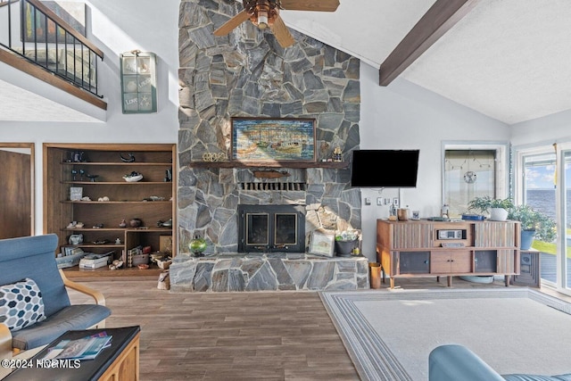 living room featuring hardwood / wood-style floors, lofted ceiling with beams, a stone fireplace, ceiling fan, and built in shelves