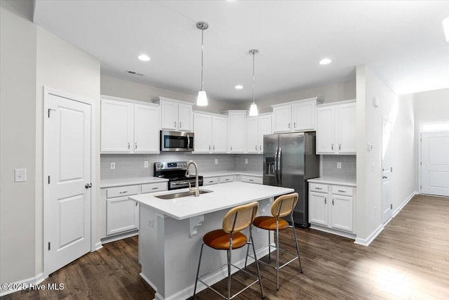 kitchen with white cabinetry, a kitchen island with sink, pendant lighting, decorative backsplash, and appliances with stainless steel finishes