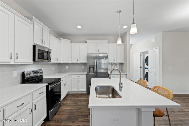 kitchen with hanging light fixtures, sink, stacked washer and dryer, an island with sink, and appliances with stainless steel finishes