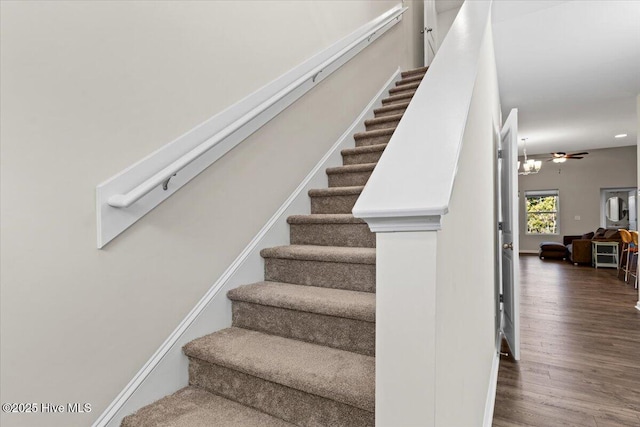 staircase featuring wood-type flooring and ceiling fan with notable chandelier