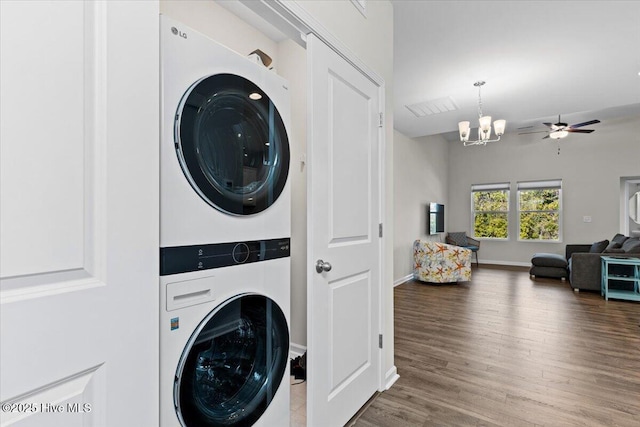 clothes washing area with hardwood / wood-style floors, stacked washer / drying machine, and ceiling fan with notable chandelier