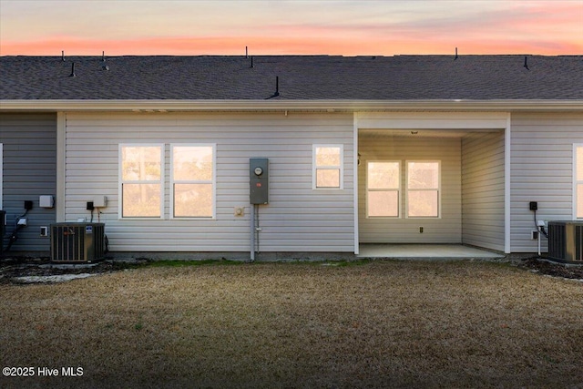 back house at dusk featuring a yard, central AC unit, and a patio area