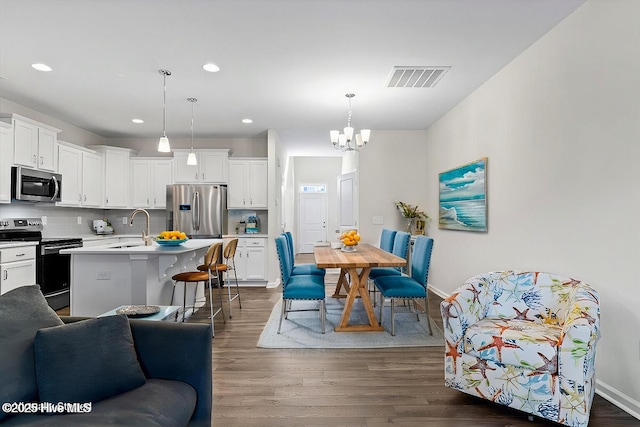 kitchen featuring white cabinetry, a center island with sink, decorative light fixtures, and appliances with stainless steel finishes