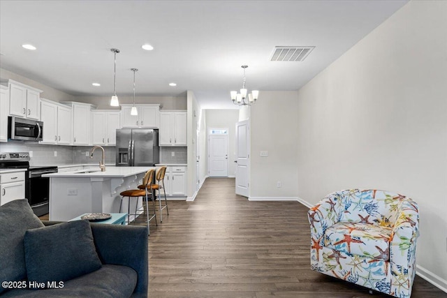 kitchen with a center island with sink, white cabinets, sink, hanging light fixtures, and appliances with stainless steel finishes