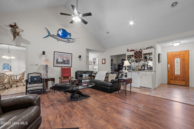 living room featuring a bar, ceiling fan with notable chandelier, light wood finished floors, and high vaulted ceiling