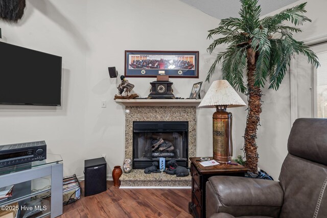 living area with a high end fireplace, vaulted ceiling, and wood finished floors