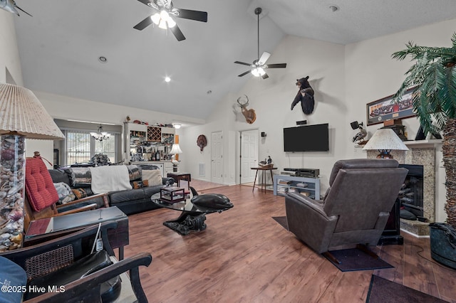 living room with a stone fireplace, ceiling fan with notable chandelier, high vaulted ceiling, and wood finished floors