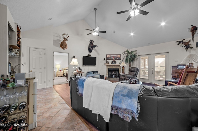 living room with a fireplace with raised hearth, french doors, light tile patterned flooring, high vaulted ceiling, and a ceiling fan