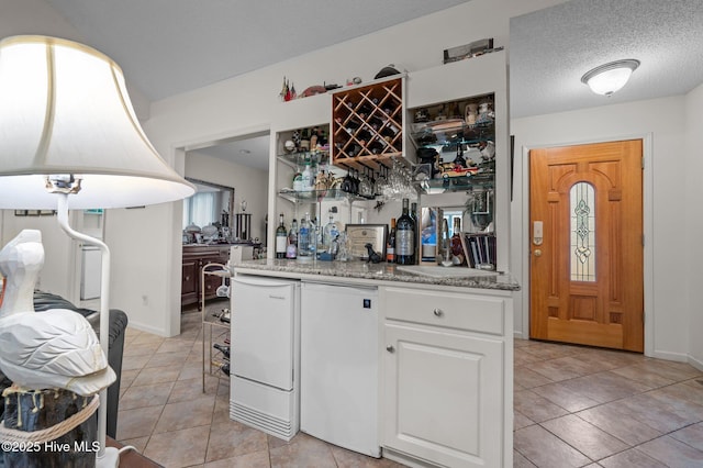 kitchen with light tile patterned floors, white cabinets, a textured ceiling, and fridge