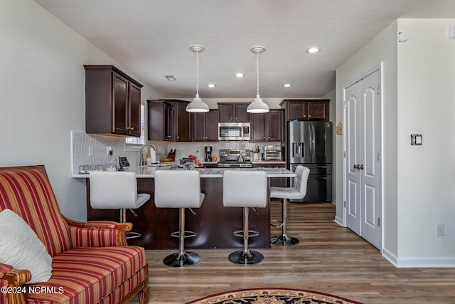 kitchen with hanging light fixtures, tasteful backsplash, light hardwood / wood-style floors, a kitchen bar, and appliances with stainless steel finishes