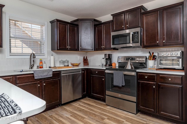 kitchen with dark brown cabinets, light wood-type flooring, sink, and appliances with stainless steel finishes