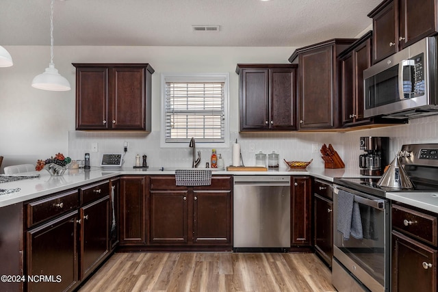 kitchen featuring sink, hanging light fixtures, light hardwood / wood-style flooring, a textured ceiling, and appliances with stainless steel finishes