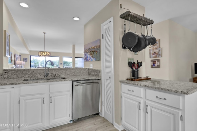 kitchen featuring white cabinets, stainless steel dishwasher, light stone countertops, and a sink