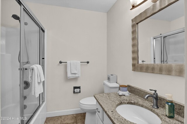 bathroom featuring toilet, combined bath / shower with glass door, tile patterned flooring, baseboards, and vanity