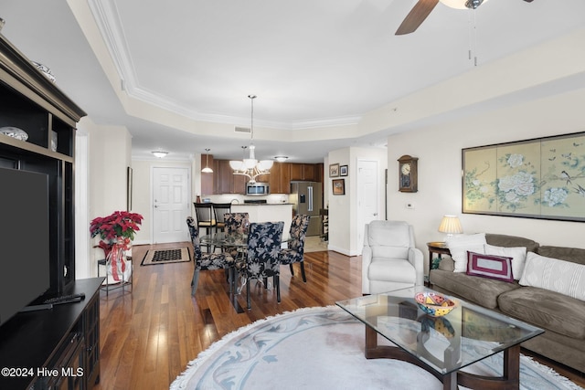 living room featuring dark hardwood / wood-style flooring, a raised ceiling, ornamental molding, and ceiling fan with notable chandelier