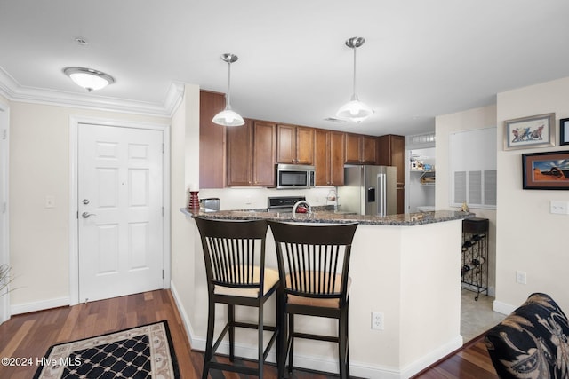 kitchen with hanging light fixtures, stainless steel appliances, kitchen peninsula, dark stone countertops, and a breakfast bar area