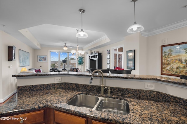 kitchen with sink, ceiling fan, dark stone countertops, a tray ceiling, and decorative light fixtures