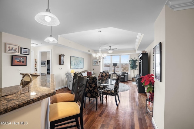 dining area with a raised ceiling, ceiling fan with notable chandelier, dark hardwood / wood-style floors, and ornamental molding