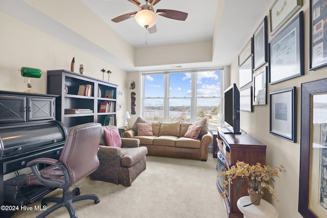 carpeted office space with a raised ceiling and ceiling fan