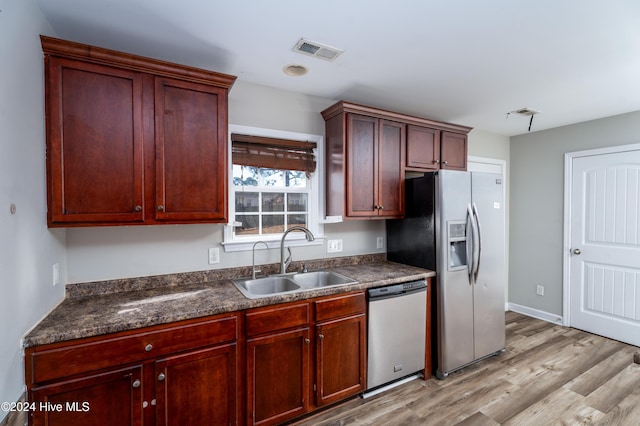 kitchen with dark stone counters, sink, stainless steel appliances, and light hardwood / wood-style floors