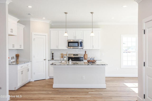 kitchen featuring light stone countertops, appliances with stainless steel finishes, decorative light fixtures, white cabinetry, and an island with sink